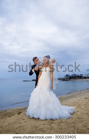 The groom is touching bridal veil of his bride. The bride looks shy.