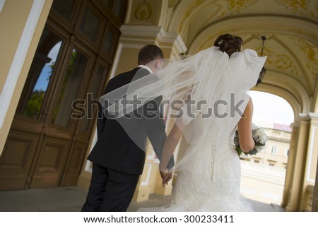Happy newlyweds are walking under church  arches. The bride is holding nice bouquet in her hand.