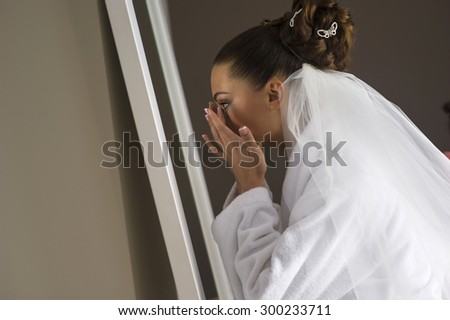 The beautiful bride is correcting her makeup. She standing in front of the mirror.