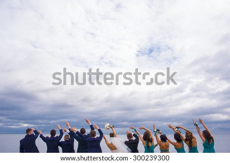 Guests on the wedding celebration are standing on the river pier, holding their hands up and looking in to the distance.