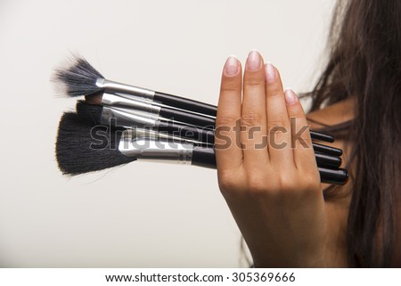 The brunette with long hair is holding makeup brush set. Nice lady in orange shirt is showing cosmetic brush set closeup.