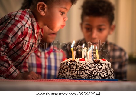 Black toddler blowing candles out. Child blows birthday candles out. Youngest brother\'s birthday. Spending festive time together.
