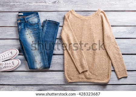 Blue jeans and beige pullover. Sweatshirt on gray wooden background. Spring casual outfit for ladies. Best items in showroom.