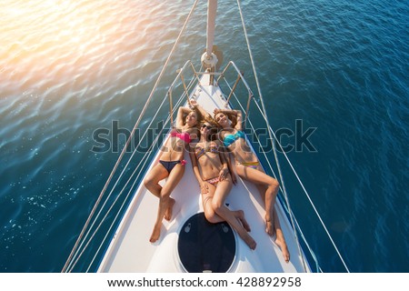 Girls lying on yacht. Smiling ladies wearing swimsuits. Have a happy summer. Today\'s weather is wonderful.
