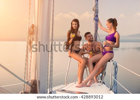 Guy with girls on yacht. People sit on yacht railing. Summer trip with friends. What a beautiful day.