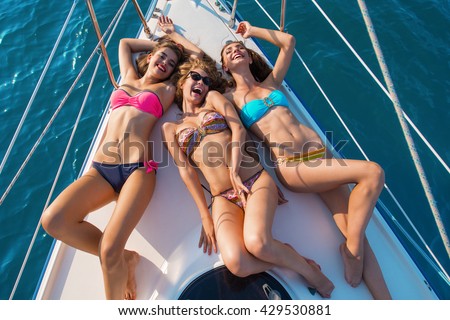 Smiling girls lying on yacht. Sexy ladies in swimsuits. Can\'t stop laughing. Summer holidays you\'ll never forget.