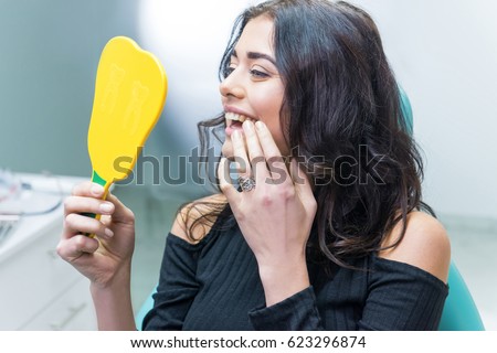 Lady checking teeth in mirror. Young female at dentist office. New dental implants.
