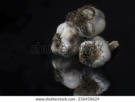 Three garlic bulbs set against a black background and placed on a black reflective surface.