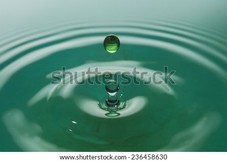 A single water drop frozen in time in a green lagoon water.