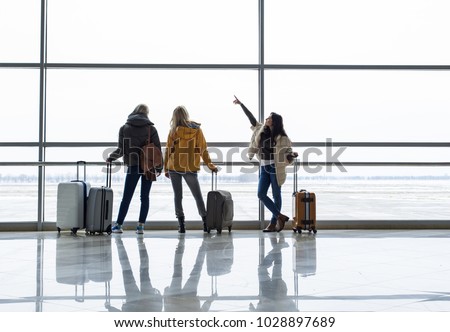 Calm girls waiting for boarding near departure gate. They are observing planes from window. Copy space in right side