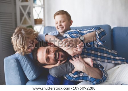 Portrait of smiling father and outgoing sons having fun on cozy couch in apartment. Happy family concept