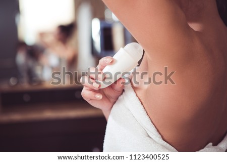 Close up of female hand preventing skin from perspiring. Girl is standing and holding antiperspirant in hand while rolling it on body