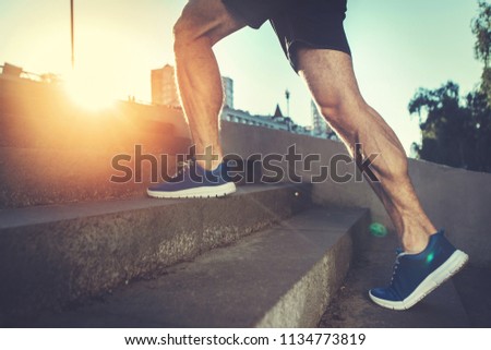 Sport hard. Close up of male feet climbing stairs outside. Well shaped man is jogging at dawn