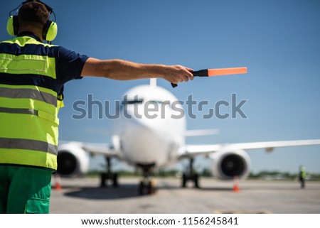 Important signal. Back view of airport worker meeting aircraft and showing right position for landing