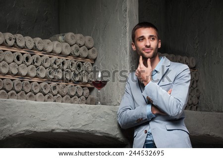 handsome man  stands in a wine cellar during tasting of wine. hands near a beard . look in left