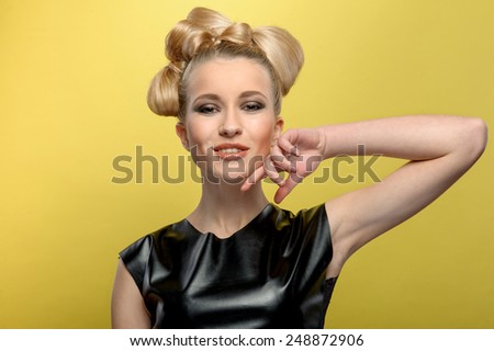 beautiful young girl with blonde hair dressed in black leather t-shirt. Smiling and looking to the camera. isolated on the yellow background