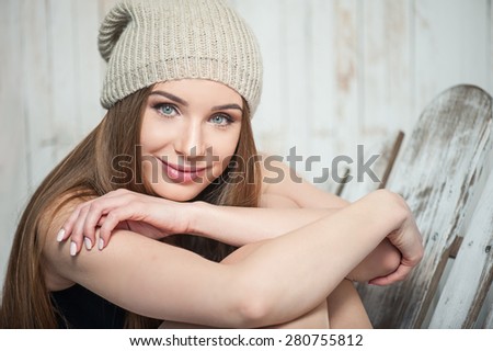 Waist up portrait of cheerful hipster girl with nice hat, who is sitting on the floor crossing her hands and looking at the camera with pretty smile and dreaming about future.