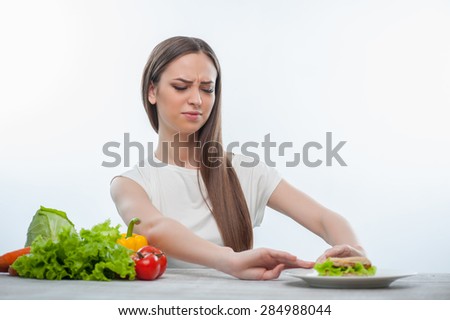 Pretty woman is refusing to eat unhealthy hamburger. She is looking at it with disgust. Isolated on a white background