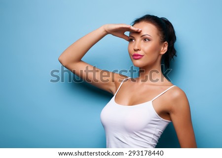 Beautiful girl is touching her hand to her forehead. She wants to watch interesting view. She is looking forward with curiosity.  Isolated on blue background