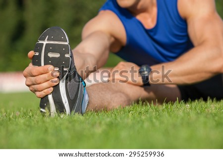 Close-up of leg of male runner stretching his leg forward. He is touching it with his hand and warming up