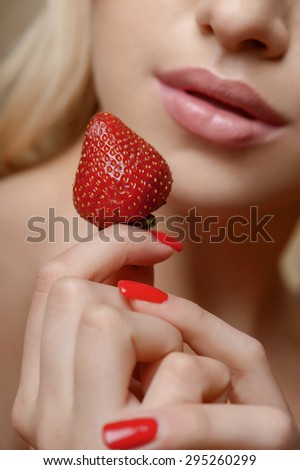Close up of strawberry hold by girl with voluptuous lips. Focus on berry