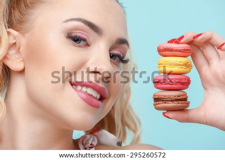 Beautiful woman is showing appetite brownies to camera. She is smiling with happiness. Isolated on blue background