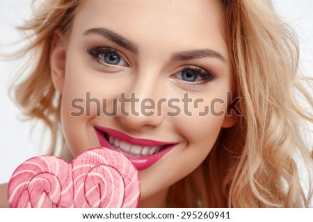 Close up of face of cheerful woman touching candy to her lips. She is smiling and looking at the camera with desire