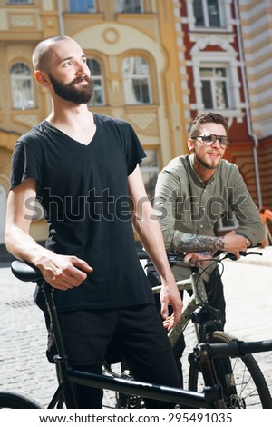 Cheerful friends are riding bicycles. They stopped to have a rest. One man is standing in profile and looking dreamingly. Another man is smiling and leaning on his transport