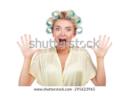 Cheerful woman is screaming and shocked. The lady is raising her arms up with great fear. She has curlers in hair. Isolated on background