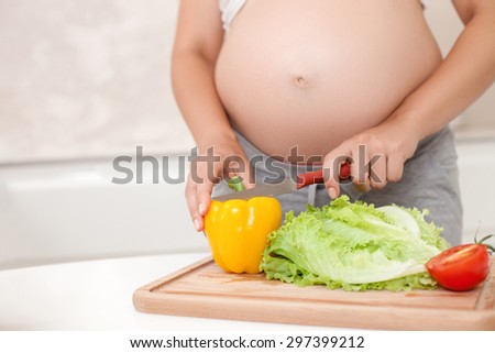 Close up of body of expectant mother cutting vegetables on the board. She is eating only healthy food. Copy space in left side