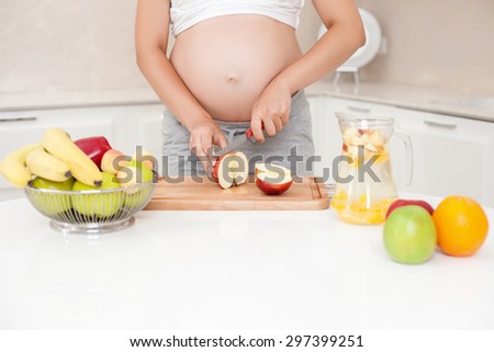 Close up of body of expectant mother chopping fruits for juice in kitchen