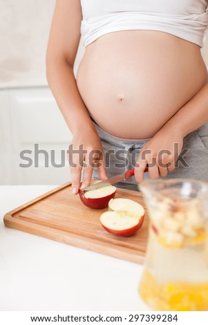 Close-up of body of pregnant woman cutting an apple for lemonade. There are a pitcher on the table