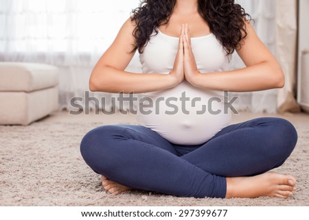 Close up of body of pregnant woman sitting on floor in lotus position. She joined her palms together