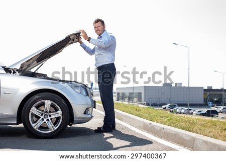 Cheerful businessman is opening car hood. He is checking the state of engine. He is smiling and looking at the camera. Copy space in right side