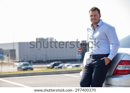 Handsome businessman is standing near his car. He is ready for traveling. He is smiling and looking at the camera. Copy space in left side