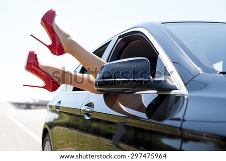 Close-up of female legs with red shoes of high heels. The woman is raising her feet through the window of the car