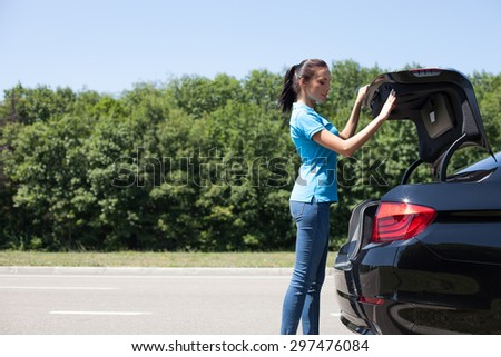 Pretty woman is opening the car trunk. She is looking inside with interest. Copy space in left side