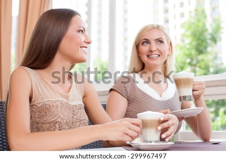 Cheerful women are spending time together with enjoyment. They are sitting at the table in cafe and talking with interest. The girls are smiling happily