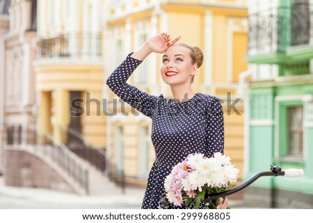 Beautiful woman is traveling with bicycle in town. She is raising her hand to her forehead and looking up with interest. The lady is smiling happily. Copy space in left side