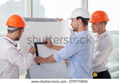Handsome architect and his colleagues are drawing sketches of building. They are taking measurements with a ruler and compass. The men are looking at the board of plan with concentration