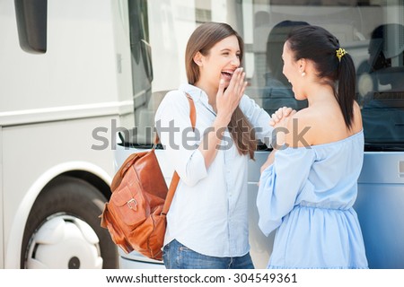 Beautiful girls are gossiping near a bus. They are waiting for bus departure. The friend are laughing and looking at each other happily