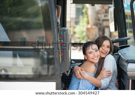 Beautiful girls are sitting on doorsteps of a bus and embracing. They are looking at the camera and smiling. Copy space in left side