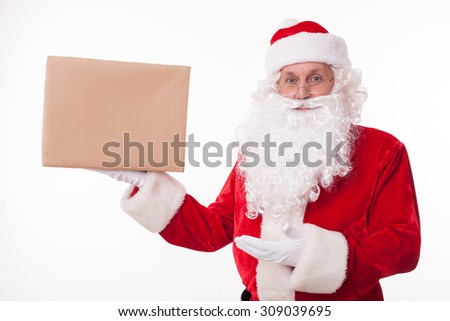 Gorgeous Santa Claus is standing and holding a box of preset. He is presenting it with another hand. The man is looking forward and smiling