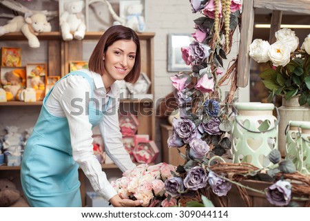 Attractive female florist is making a bouquet with inspiration. She is standing in her workshop and smiling. The lady is looking at the camera happily