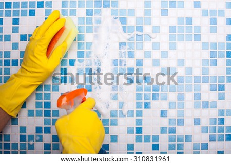 Close up of male hands washing tile in bathroom. The cleaner is spraying the wall and scrubbing it with a washcloth. The man is wearing gloves. Copy space in right side