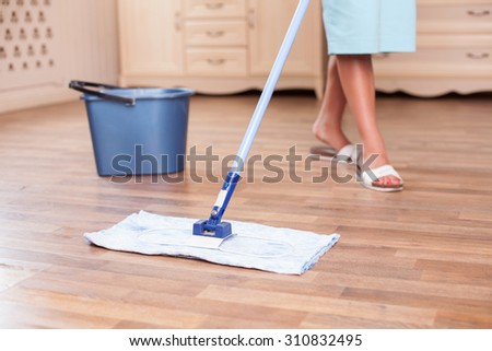 Close up of legs of female cleaner mopping flooring. The woman is standing near a bucket