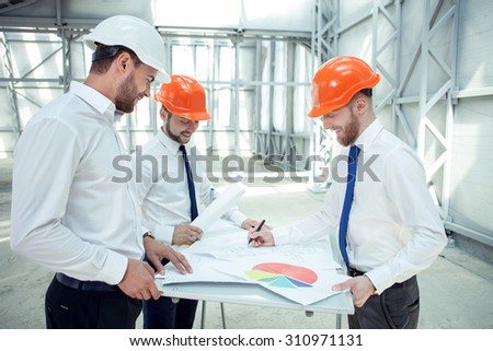 Pretty architects are discussing the plan of constructing. The man is drawing sketches on the blueprint and smiling. His colleagues are looking at it with joy