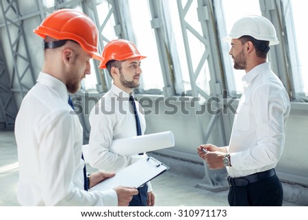 Cheerful architect and builders are talking about their new project with inspirations. They are looking at each other and smiling. The foremen is holding the folder and reading with concentration