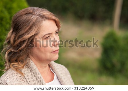 Pretty old woman is standing and resting in park. She is dreaming and looking aside pensively. Copy space in right side