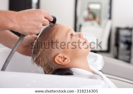 Cheerful male child is having his hair washed in Hair salon. He is leaning his head on sink. The kid is looking up with joy